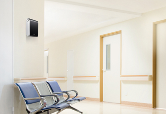 진료실과 같은 의료시설 내 벽면에 장소별 맞춤형 설계가 가능한 세스코(CESCO)의 공간 방향기 에어퍼퓸 제품이 설치되어 있고 하단에는 의자가 놓여있습니다.